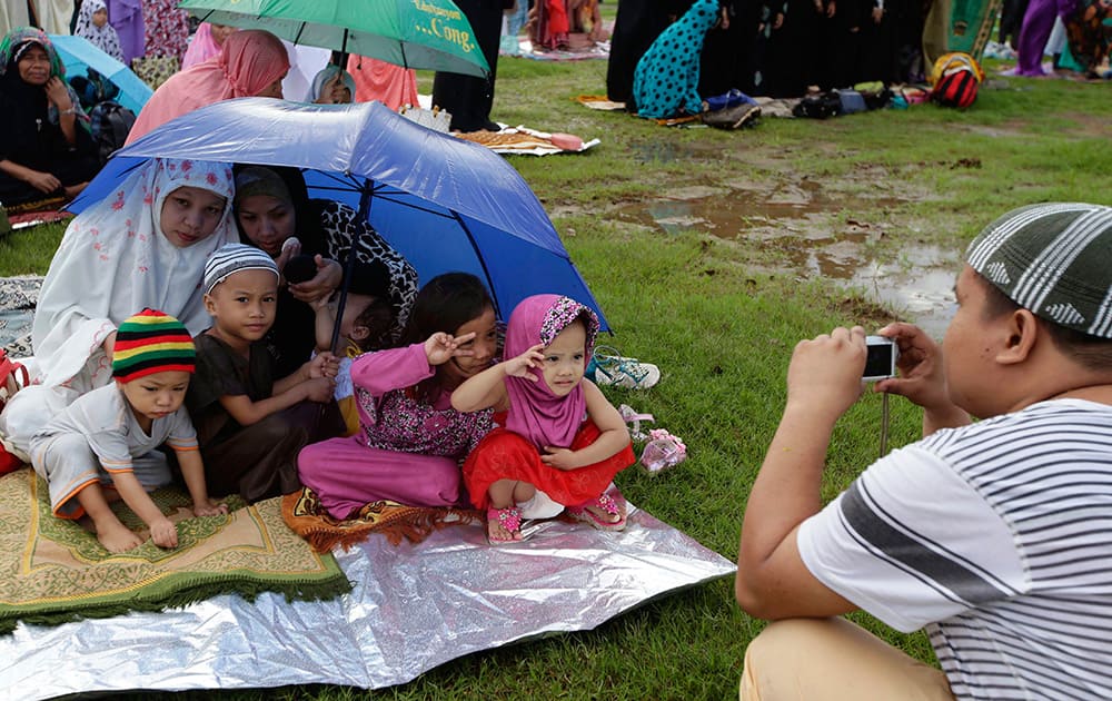 A Filipino Muslim father takes souvenir photos of his family as they gather at Rizal Park to pray in celebration of Eid al-Fitr marking the end of the holy month of Ramadan in Manila, Philippines.