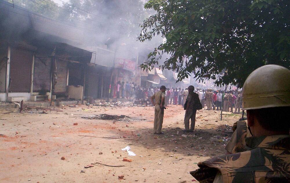 Security men stad guard in a street as brick-bats are lying on the road after violent clashes between two communities over a land dispute in Saharanpur.