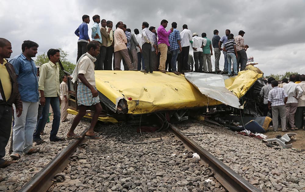 People stand on top of a bus that was crushed when a train crashed into it in Medak district in Telangana. Twelve children were killed Thursday when a train crashed into a school bus at an unmanned railroad crossing.