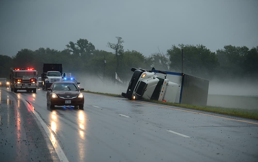 A tractor trailer truck lies on its side in the median of U.S. Route 13 in Cheriton, Va. while a fire engine responds to a nearby campground after a severe storm passed through the area.