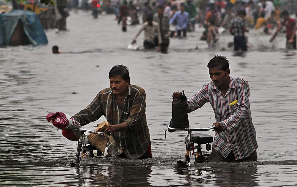 Indian men push their bicycles as they wade through a water- logged area after heavy monsoon rains in Ahmedabad.