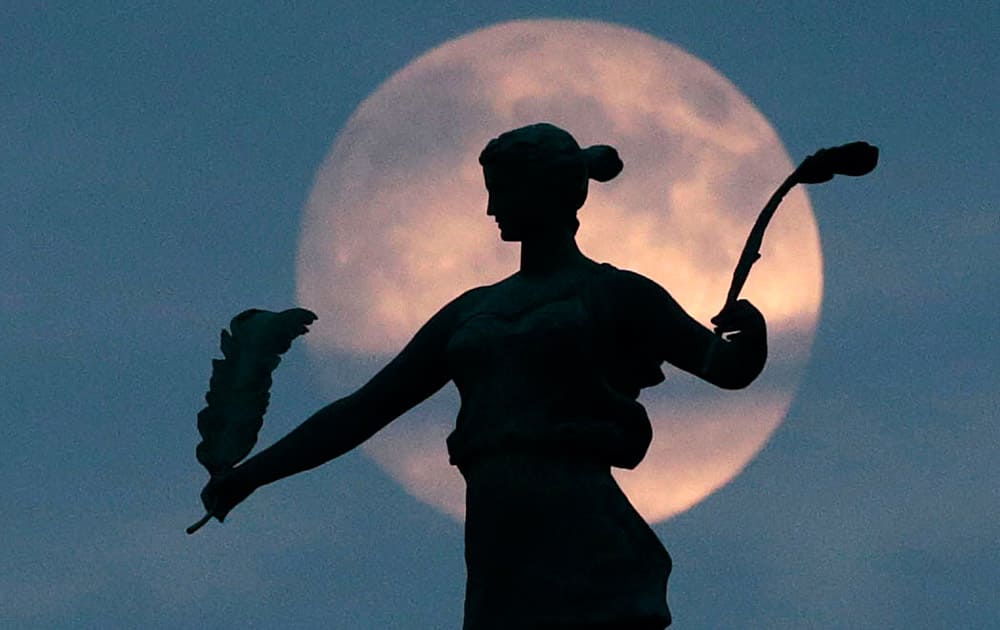 The moon is seen as it rises over a statue by Harriet A. Ketcham titled