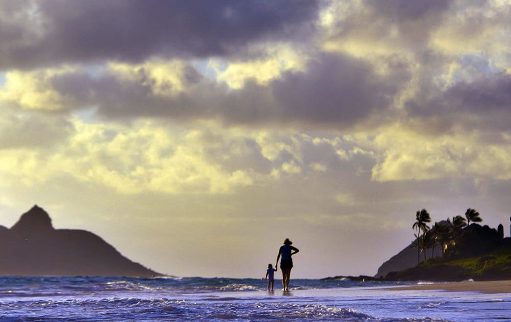 Anne Kllingshirn, of Kailua, Hawaii walks with her daughter Emma, 1, as storm clouds float overhead during the sunrise hours on Kailua Beach, in Kailua, Hawaii.