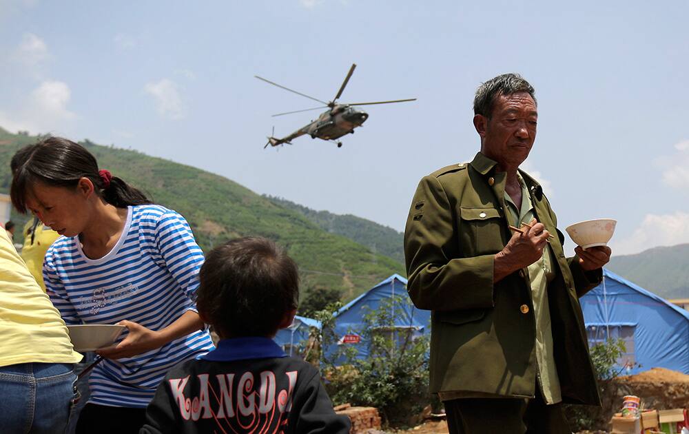 A helicopter flies past villagers receiving food from volunteers at tents set up for earthquake survivors in Longtoushan town in Ludian county in southwest China`s Yunnan province.