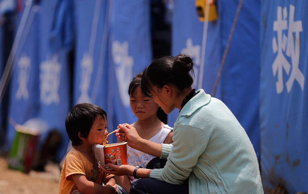 A woman feeds instant noodle to the children outside a temporary tent set up for the earthquake survivors in the town of Longtoushan in Ludian County in southwest China`s Yunnan Province.