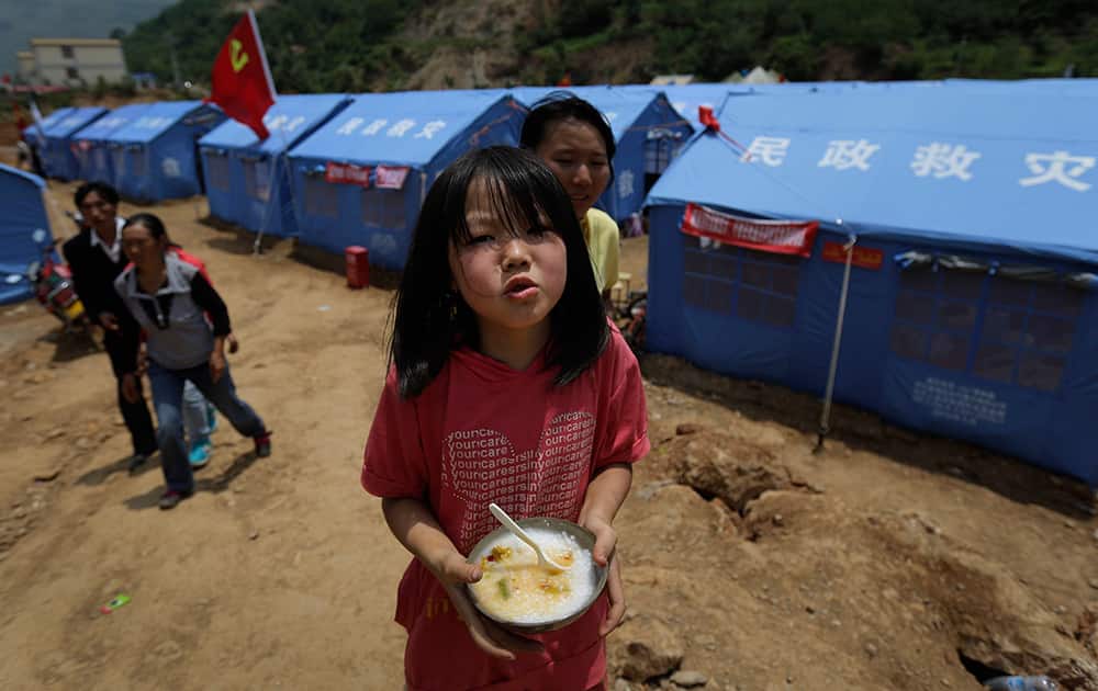 A child holds a bowl of porridge cooked by volunteers in front of temporary tents set up at the quake-hit area in the town of Longtoushan in Ludian county in southwest China`s Yunnan Province.