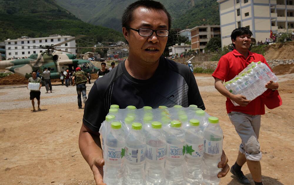 Volunteers deliver bottles of water transported by a helicopter to the earthquake hit Longtoushan town in Ludian county in southwest China`s Yunnan province .