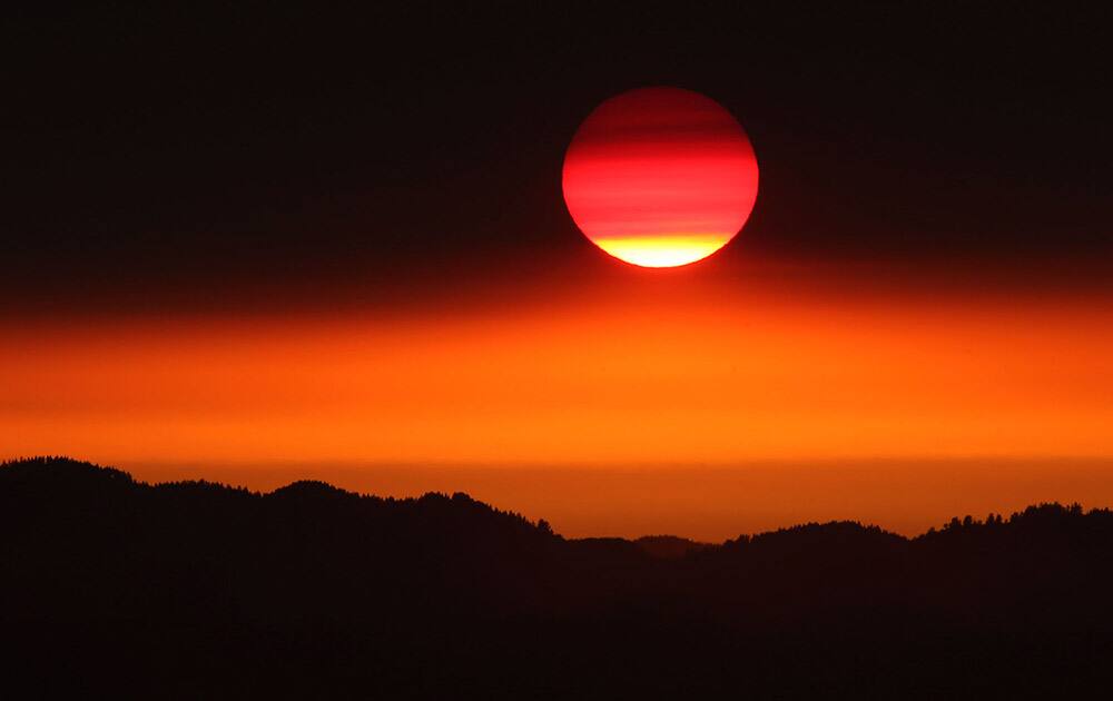 The Sun begins to peek out from below a layer of smoke blowing north from fires in southern Oregon and Northern California as it sets on the Willamette Valley near Eugene, Ore.