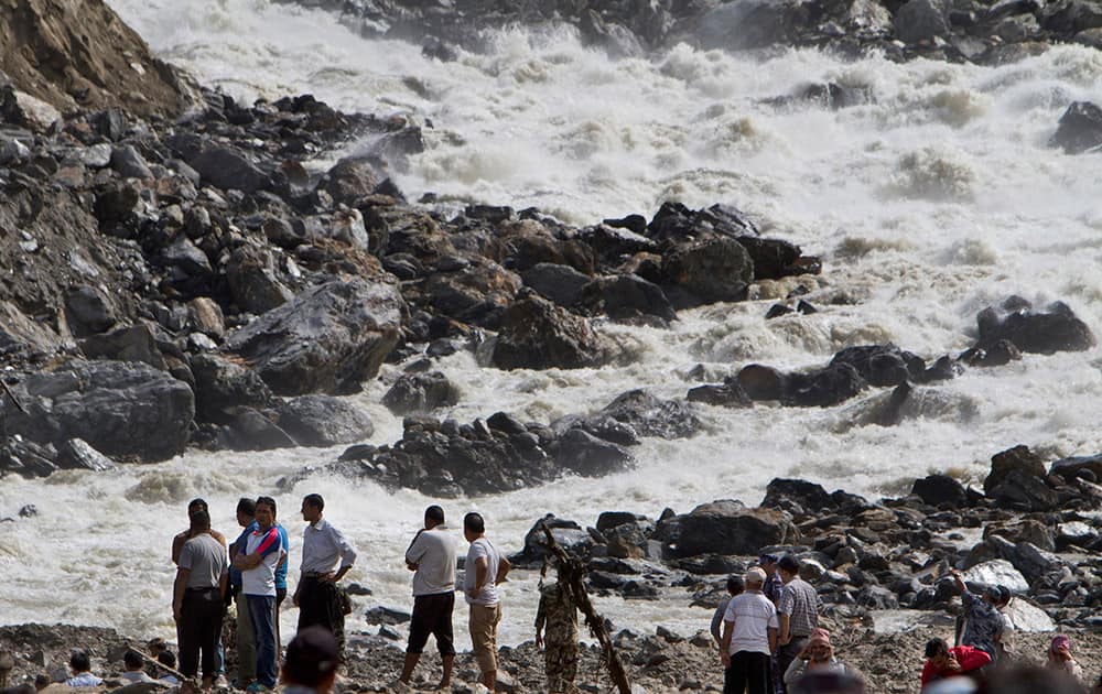 People stand at the banks of the River Sunkoshi near the site of a massive landslide in Mankha village, about 120 kilometers (75 miles) east of Katmandu, Nepal.