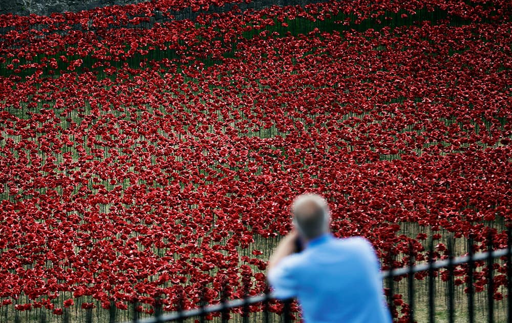 A man looks at ceramic poppies forming part of an art installation in the dry moat of the Tower of London in London. The installation of 888,246 ceramic poppies by ceramic artist Paul Cummins entitled `Blood Swept Lands and Seas of Read` will be unveiled on August 5 to mark the centenary of World War I, with the final one being planted on Armistice Day on November 11. Each poppy represents a British military fatality from World War I.