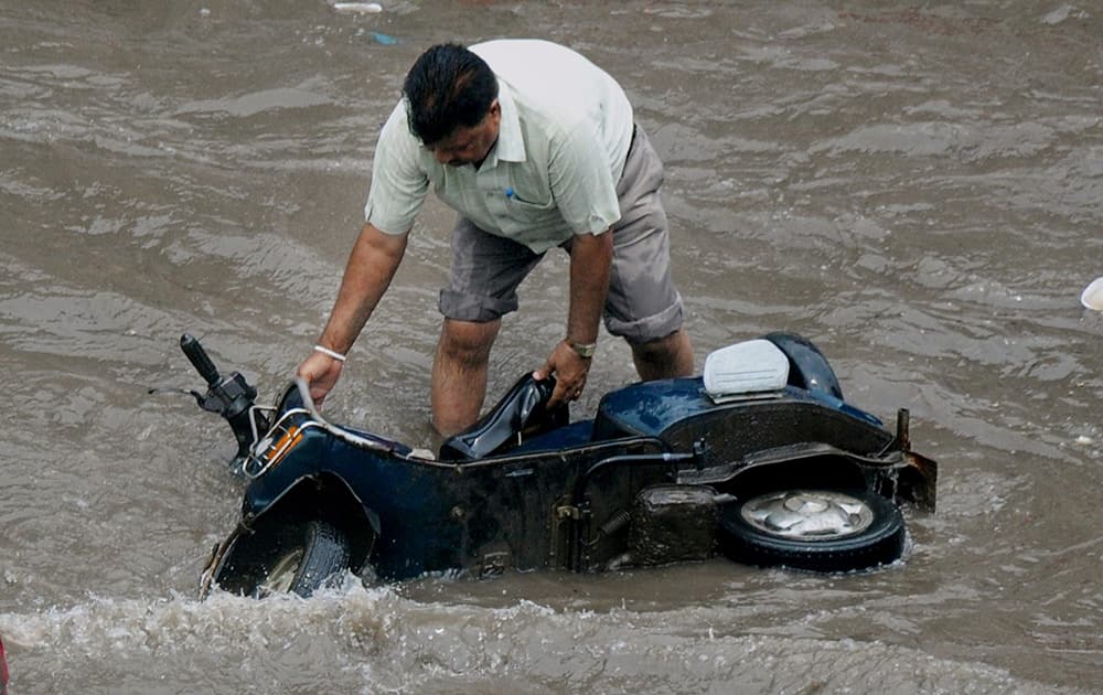 A man trying to put his scooter in upright position after it fell at a waterlogged road in Amritsar.