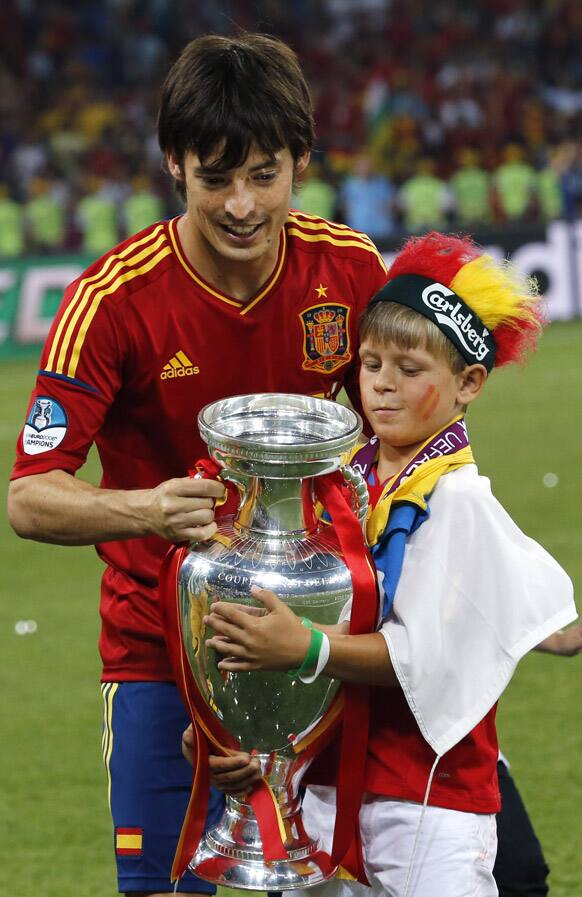 Spain's David Silva celebrates with a boy, holding the trophy after during the Euro 2012 soccer championship final between Spain and Italy in Kiev, Ukraine.