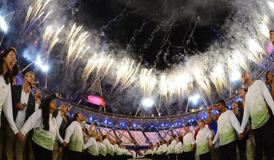 Athletes and volunteers watch a fireworks display after the Olympic cauldron was lit during the Opening Ceremony at the 2012 Summer Olympics in London.