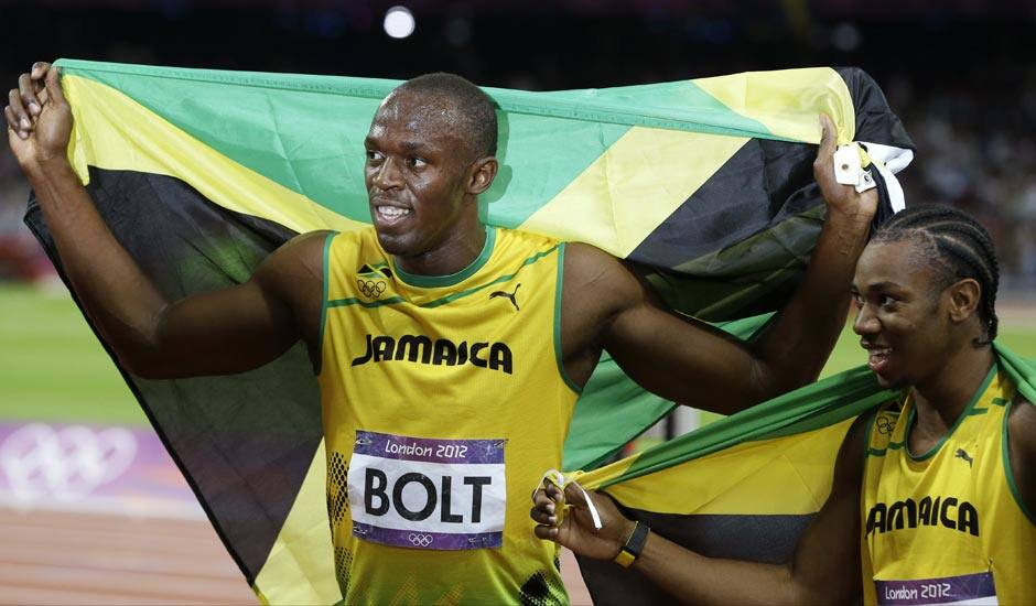 Usain Bolt, left, holds his national flag as teammate Yohan Blake, right, poses with him after Bolt's win in the men's 100-meter final during the athletics in the Olympic Stadium at the 2012 Summer Olympics.