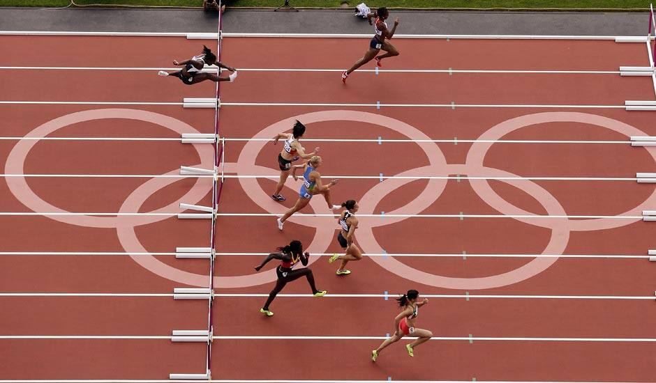 Runners clear a hurdle during round 1 of the women's 100-meter hurdles during the athletics in the Olympic Stadium at the 2012 Summer Olympics.