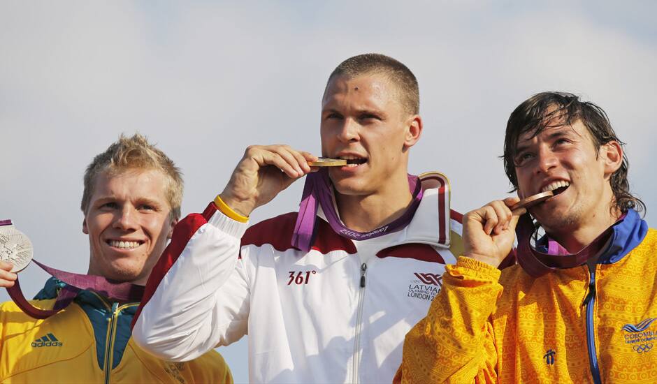 Latvia's Maris Strombergs, bites his gold medal with silver medalist, Sam Willoughby, of Australia, and bronze medalist Carlos Mario Oquendo Zabala, of Colombia, during the 2012 Summer Olympics in London.