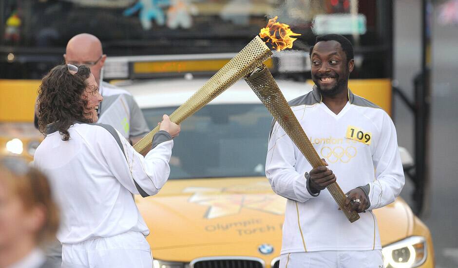 Will.i.am of the Black Eyed Peas passes the Olympic Flame to torchbearer Emma Fowler in Taunton, England