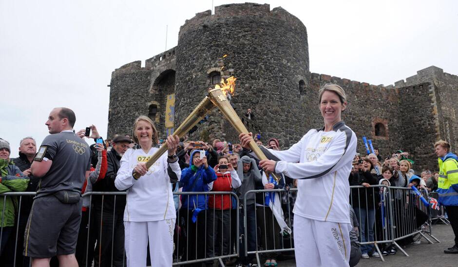 Kathleen Irvine, left, passes Lisa Hickson the Olympic Flame outside of Carrickfergus Castle in Carrickfergus Northern Ireland during the Olympic Torch Relay.