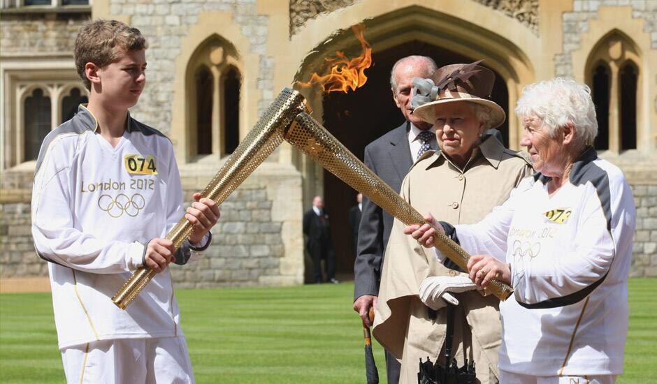 This image made available by LOCOG shows Queen Elizabeth II, second right, and the Duke of Edinburgh watching the Torch Kiss as Torchbearer 073 Gina Macgregor, right, passes the Olympic Flame to Torchbearer 074 Phillip Wells, left, outside Windsor Castle, Windsor, England