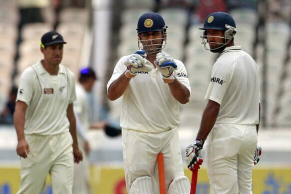 Mahendra Singh Dhoni, center, gestures as he stands next to Cheteshwar Pujara during the second day of the first cricket test match against New Zealand in Hyderabad.