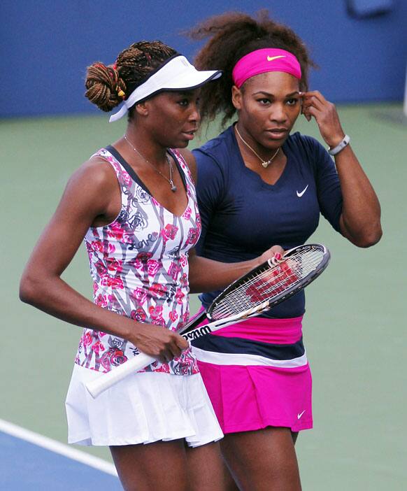 Venus and Serena Williams talk while playing a doubles match in the second round of play at the 2012 US Open tennis tournament.