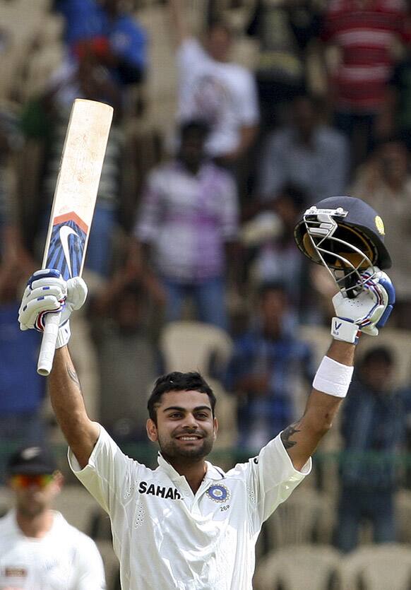 Virat Kohli raises his bat and helmet to celebrate scoring a century during the third day of their second cricket test match against New Zealand in Bangalore.