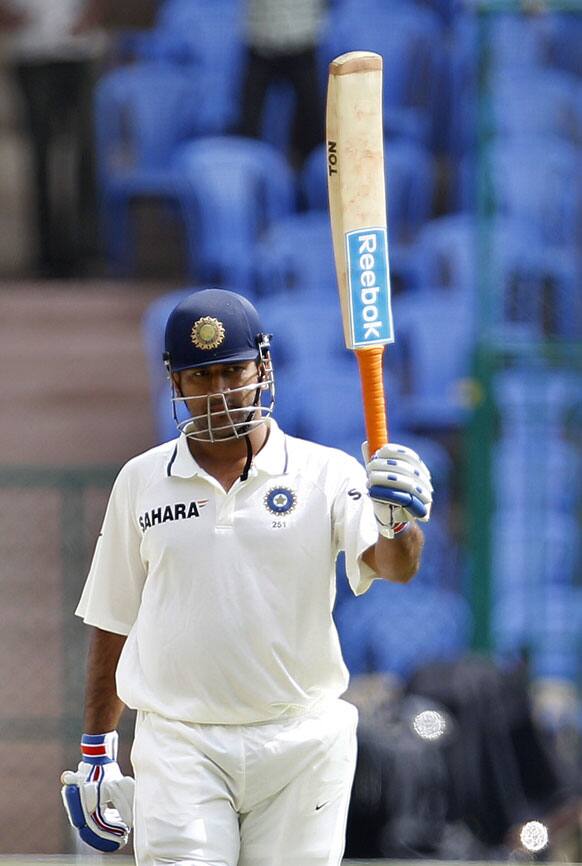 Mahendra Singh Dhoni raises his bat to celebrate scoring a half-century during the third day of their second cricket test match against New Zealand in Bangalore.