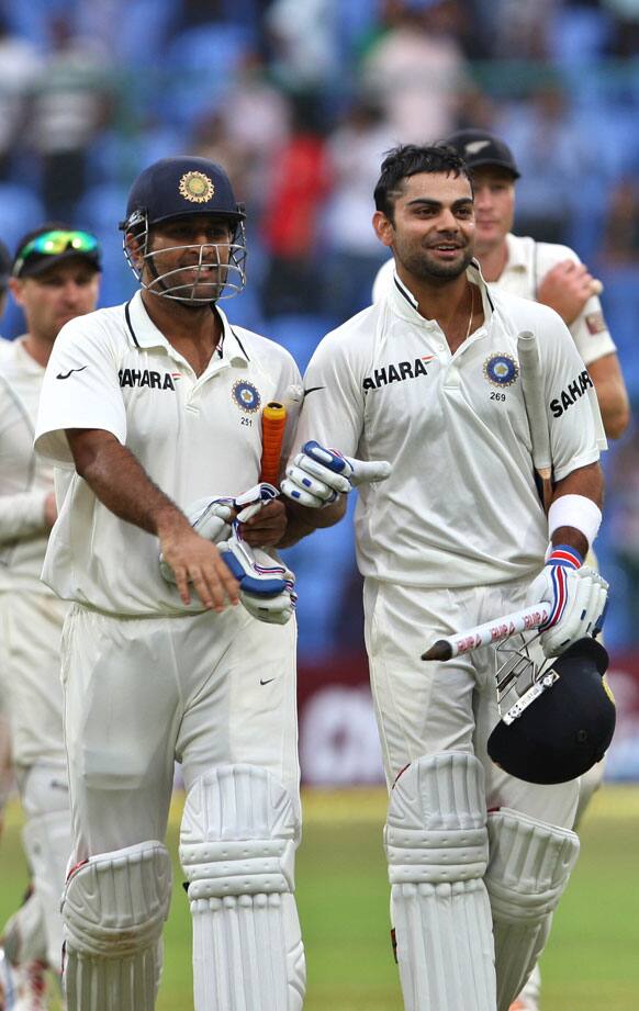 Mahendra Singh Dhoni, left, and teammate Virat Kohli, right, leave the ground as they celebrate their win over New Zealand on the fourth day of their second cricket test match in Bangalore.