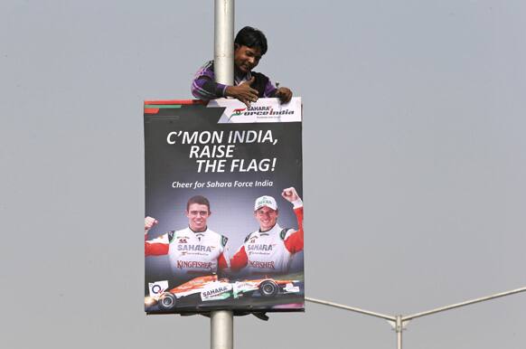 An Indian worker pus up a poster of Formula One Force India drivers Nico Hülkenberg, right, and Paul Di Resta, beside a road leading to Buddh International Circuit in Noida, on the outskirts of New Delhi.