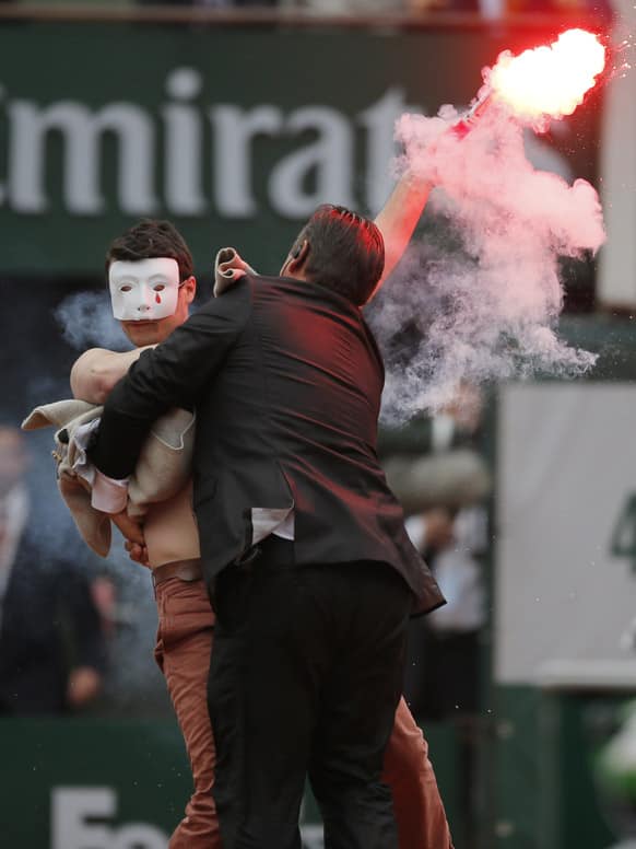 A security guard grabs a demonstrator as Spain's Rafael Nadal plays against compatriot David Ferrer in the final of the French Open tennis tournament, at Roland Garros stadium in Paris.