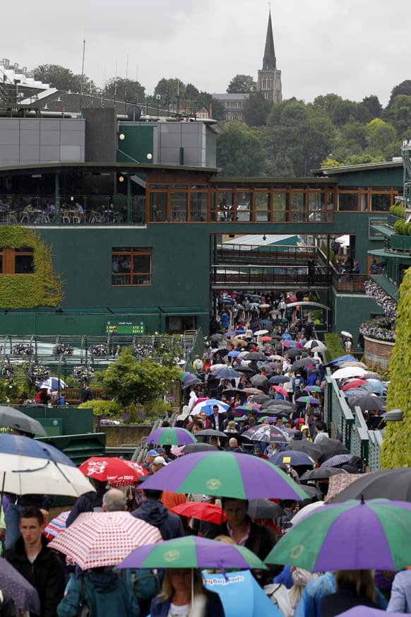 Members of the public seek shelter under umbrellas as rain delays the start of play at the All England Lawn Tennis Championships in Wimbledon.