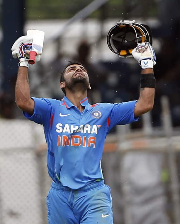 Virat Kohli raises his bat and helmet after scoring a century during the Tri-Nation Series cricket match against the West Indies in Port-of-Spain, Trinidad.