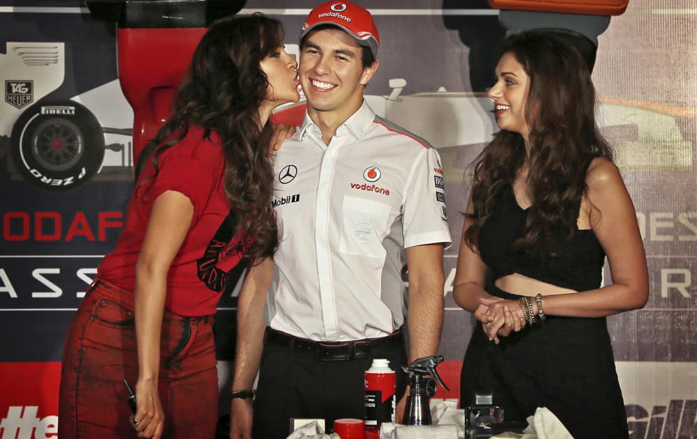 Bollywood actress Neha Dhupia kisses the cheek of McLaren Formula One driver Sergio Perez of Mexico as Aditi Rao Hydari stands beside him during a promotional event, in New Delhi.