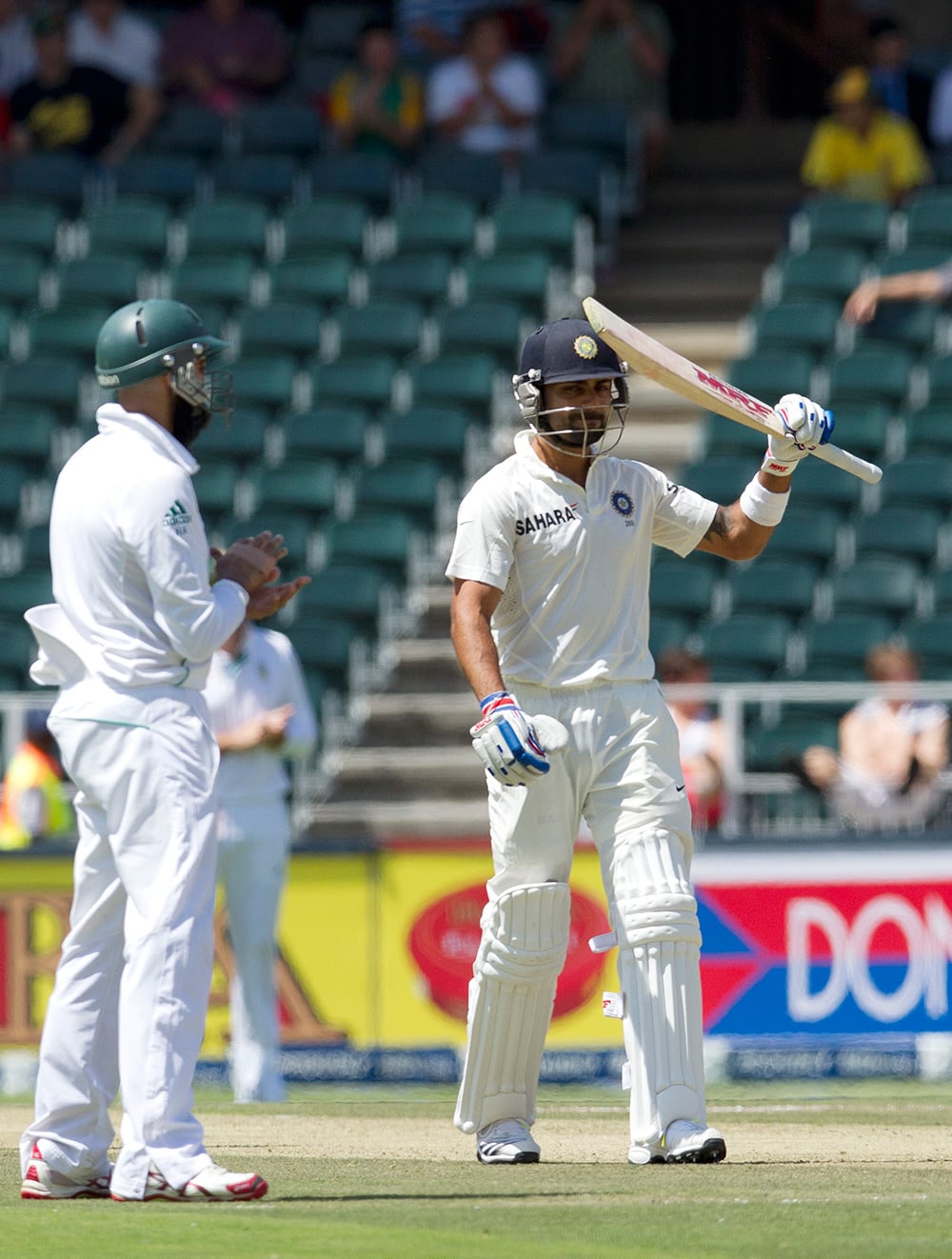 Virat Kohli raises his bat after reaching half century as South Africa's Hashim Amla claps hands during the first day of their cricket test match at Wanderers stadium in Johannesburg, South Africa.