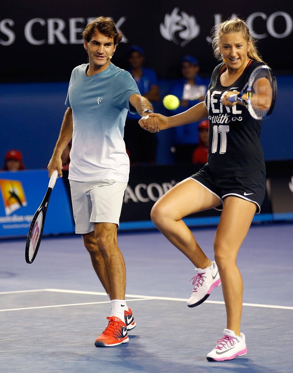 Victoria Azarenka of Belarus plays a shot as she holds hands with Switzerland's Roger Federer during an exhibition match on Kids Tennis Day ahead of the Australian Open tennis championship in Melbourne.