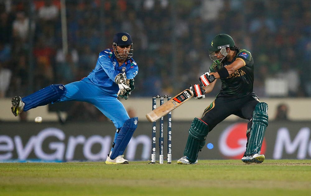 Pakistan's batsman Umar Akmal, right, plays a shot as India's captain Mahendra Singh Dhoni reacts during their ICC Twenty20 Cricket World Cup match in Dhaka, Bangladesh.