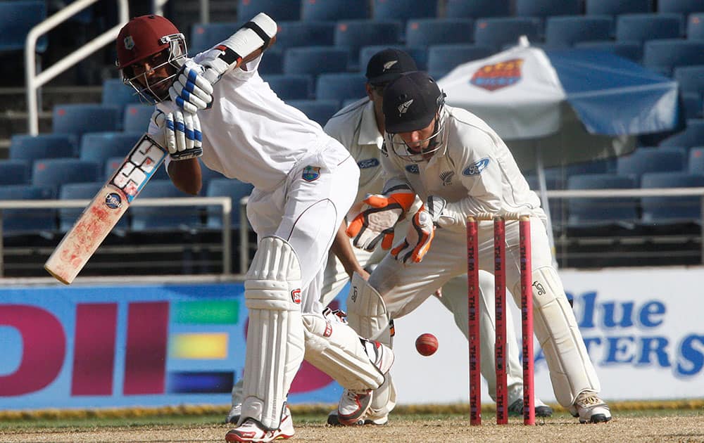 West Indies captain Denesh Ramdin, left, plays a shot as New Zealand's wicket keeper Brendon McCullum looks on during the second innings on the fourth day of their first cricket Test match in Kingston, Jamaica.