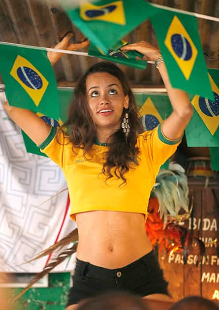 A woman dressed in the colors of the Brazilian flag touches the corrugated ceiling as she dances on the bar while soccer fans watched the first game of the 2014 World Cup at Miss Favela, a packed-to-capacity Brazilian bar in the Williamsburg section of New York.