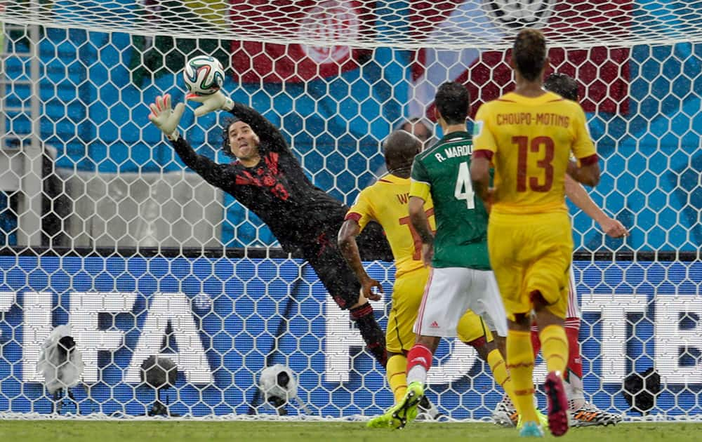 Mexico's goalkeeper Guillermo Ochoa, left, dives to make a save during the group A World Cup soccer match between Mexico and Cameroon in the Arena das Dunas in Natal, Brazil.