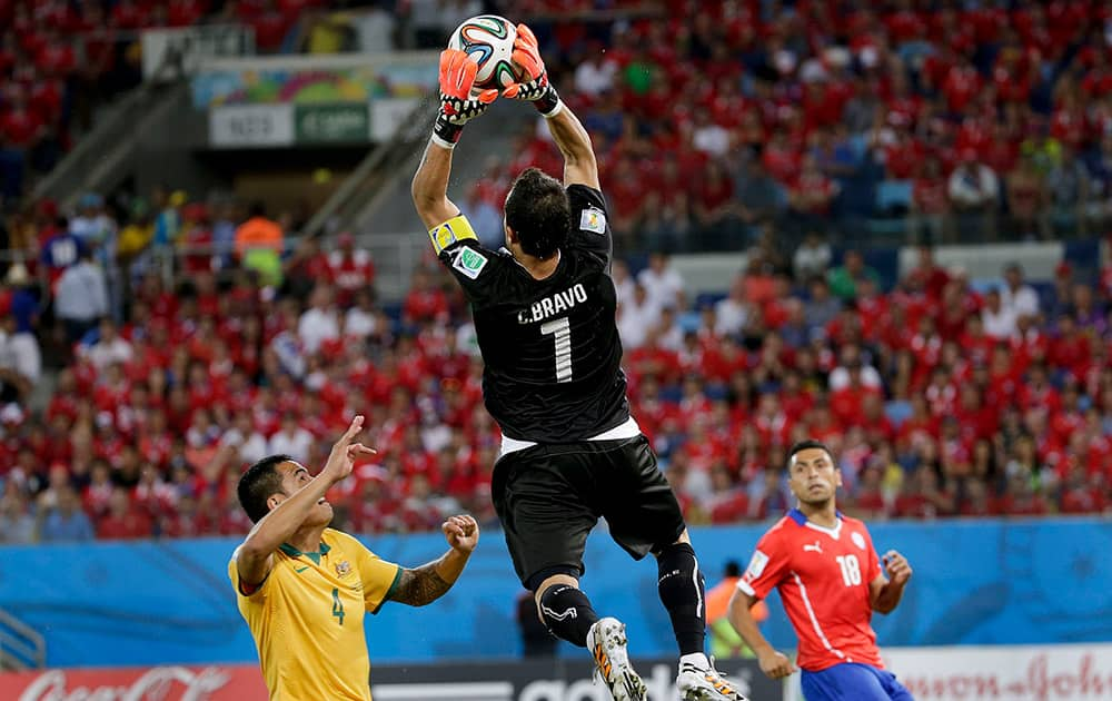 Chile's goalkeeper Claudio Bravo leaps above Australia's Tim Cahill to claim the ball during the group B World Cup soccer match between Chile and Australia at the Arena Pantanal in Cuiaba, Brazil.