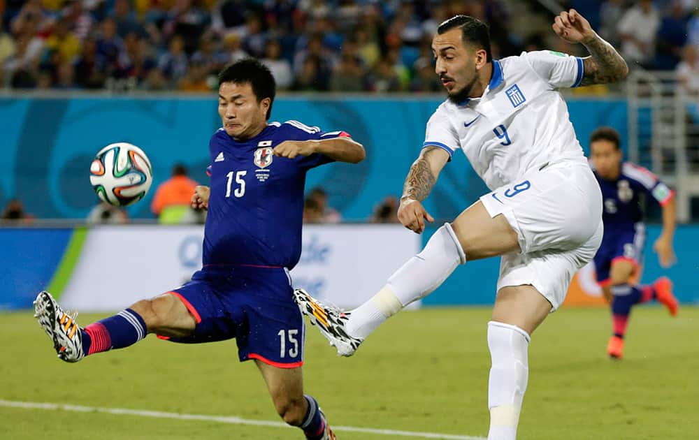 Greece's Kostas Mitroglou, right, gets a shot off in front of Japan's Yasuyuki Konno during the group C World Cup soccer match between Japan and Greece at the Arena das Dunas in Natal, Brazil.