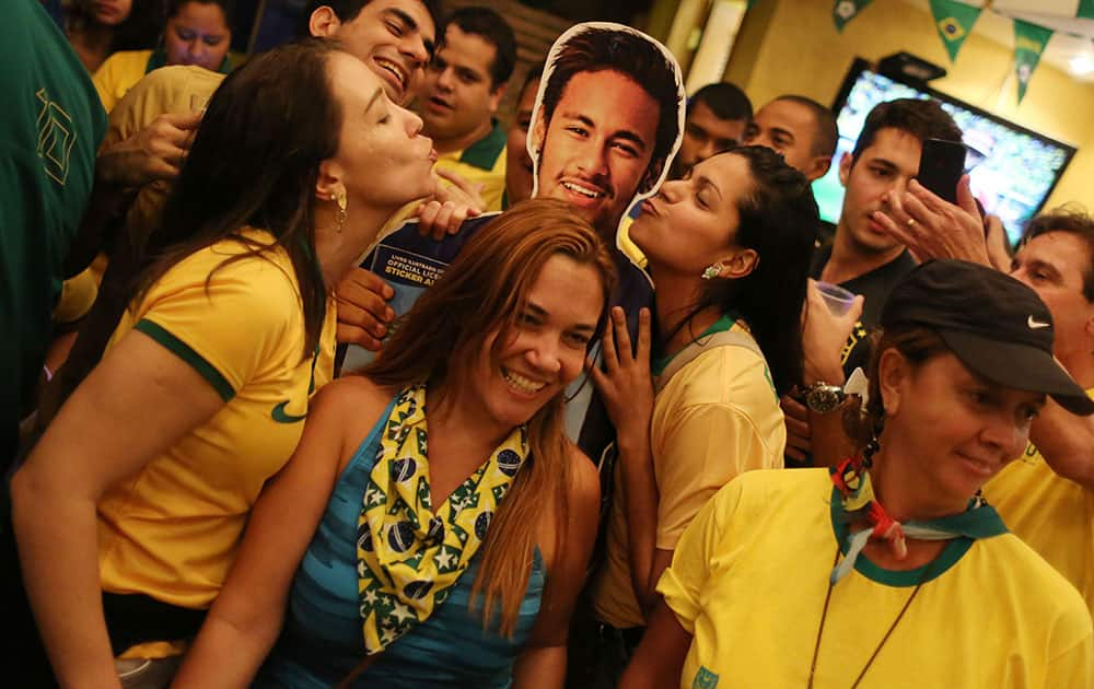 Soccer fans donning Brazil's national team colors pose for a picture with a life-size cutout of soccer star Neymar, after the World Cup match between Brazil and Cameroon, at the Copacabana beach, in Rio de Janeiro, Brazil.