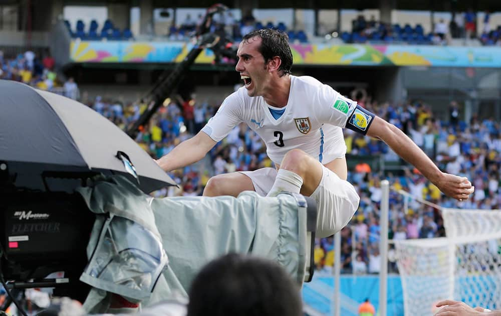 Uruguay's Diego Godin leaps over a barricade next to a television camera as he celebrates after scoring his side's first goal during the group D World Cup soccer match between Italy and Uruguay at the Arena das Dunas in Natal, Brazil.