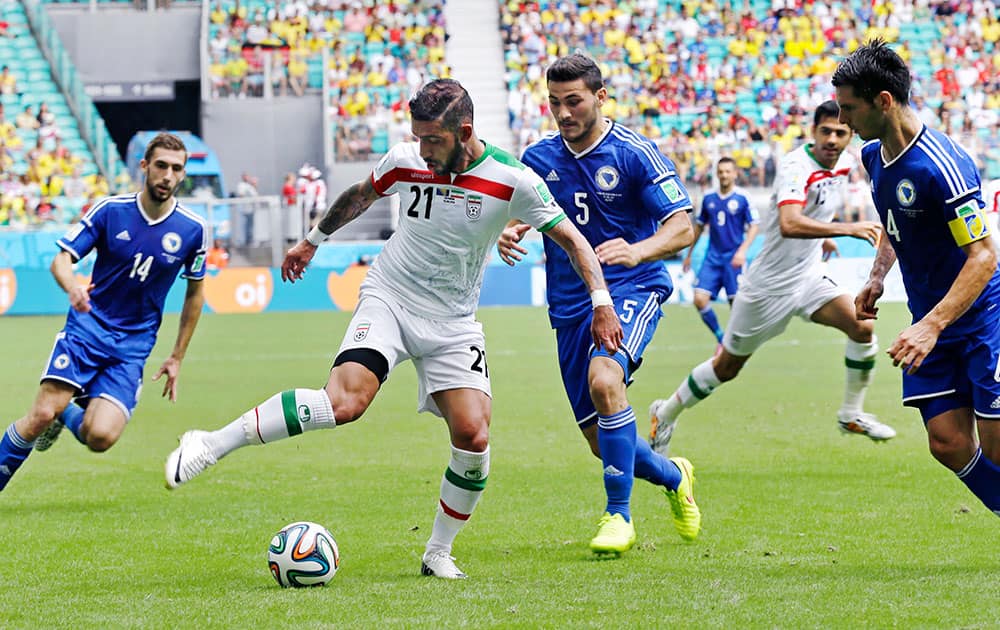 Iran's Ashkan Dejagah shoots a pass to Iran's Pejman Montazeri, rear, through Bosnia's Sead Kolasinac (5) and Emir Spahic (4), during the group F World Cup soccer match between Bosnia and Iran at the Arena Fonte Nova in Salvador, Brazil.