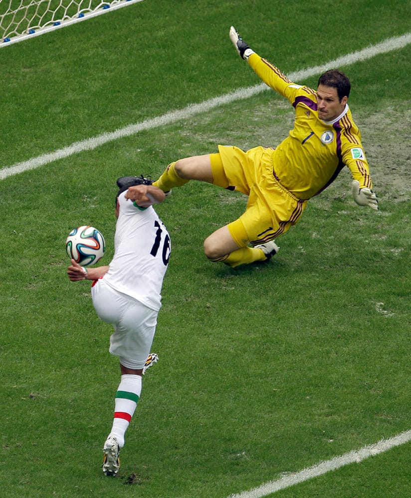 Bosnia goalie Asmir Begovic, top, blocks a shot by Iran forward Reza Ghoochannejhad during the first half of a group F World Cup soccer match at the Arena Fonte Nova in Salvador, Brazil.