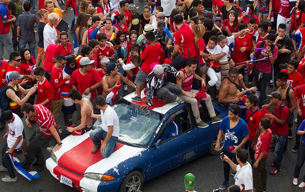 Costa Rica soccer fans gather around a car painted in the colors of the nation's flag as they celebrate their team's victory over Greece at a Brazil World Cup round of 16 game in San Jose, Costa Rica.