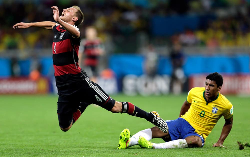 Germany's Benedikt Hoewedes (4) is tripped by Brazil's Paulinho (8) during the World Cup semifinal soccer match between Brazil and Germany at the Mineirao Stadium in Belo Horizonte, Brazil.