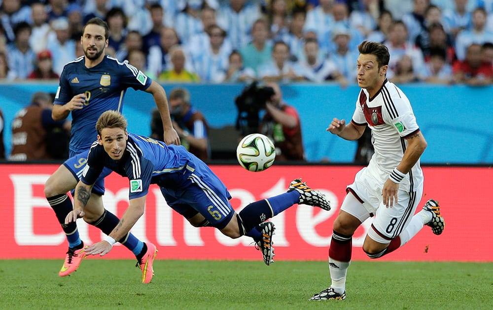 Argentina's Lucas Biglia, center, heads the ball clear from Germany's Mesut Ozil, right, during the World Cup final soccer match between Germany and Argentina at the Maracana Stadium in Rio de Janeiro.