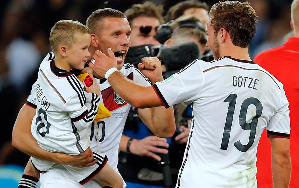 Germany's Lukas Podolski holds is son as he celebrates with Mario Goetze, right, after the World Cup final soccer match between Germany and Argentina at the Maracana Stadium in Rio de Janeiro, Brazil