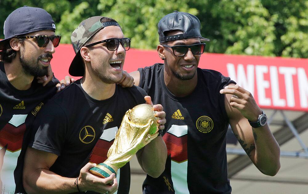 Sami Khedira, Lukas Podolski and Jerome Boateng celebrate with trophy during a fan party after the arrival of the German national soccer team in Berlin.